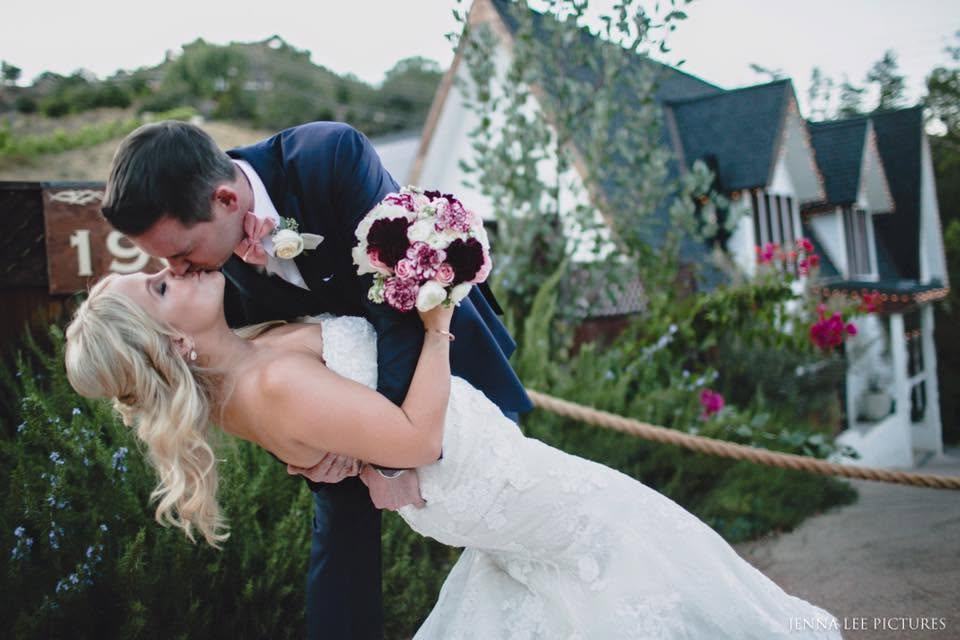 Groom dipping the bride for a kiss outside a garden cottage